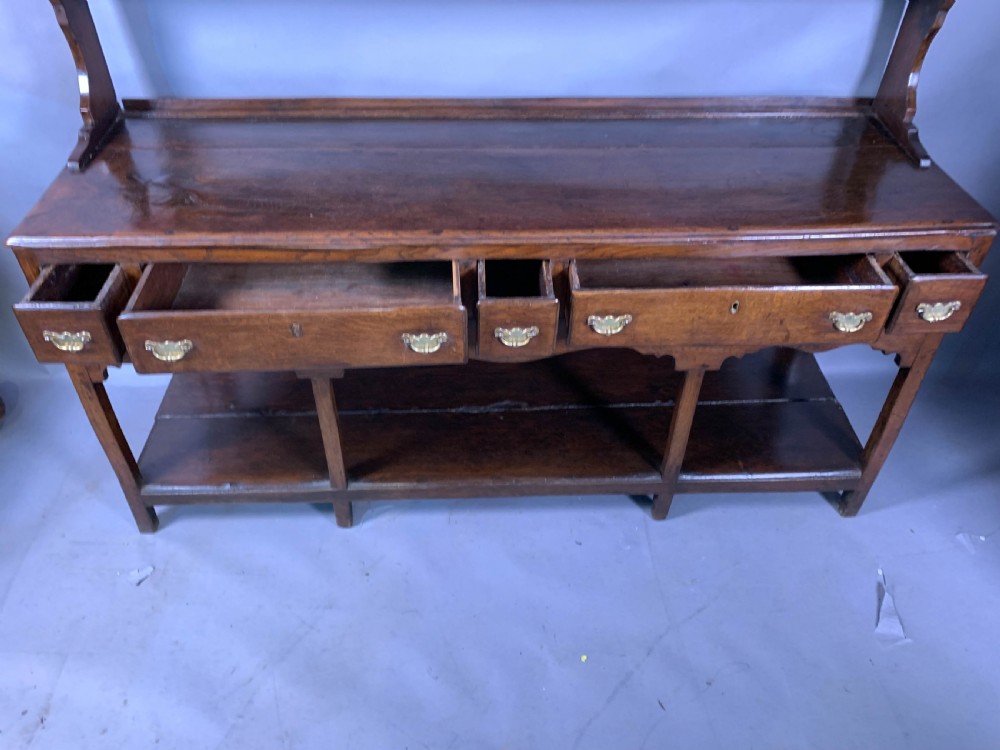 An 18th-century oak Welsh dresser featuring an open rack top with plate hooks, a central base with multiple drawers, and a lower pot board shelf. View IX