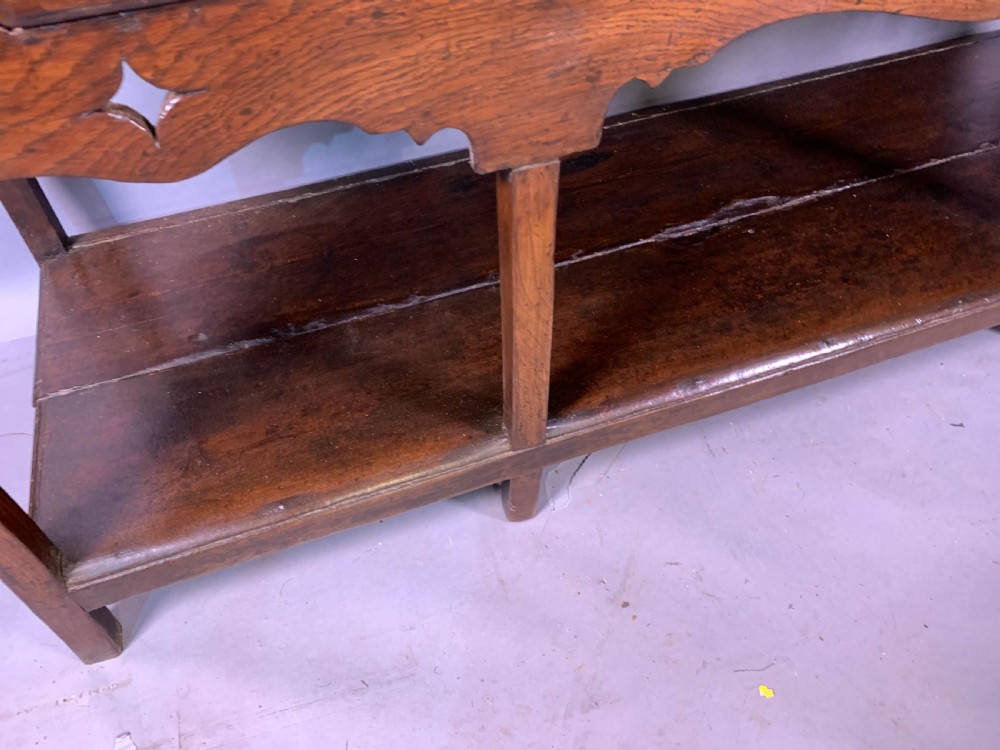 An 18th-century oak Welsh dresser featuring an open rack top with plate hooks, a central base with multiple drawers, and a lower pot board shelf. View XV