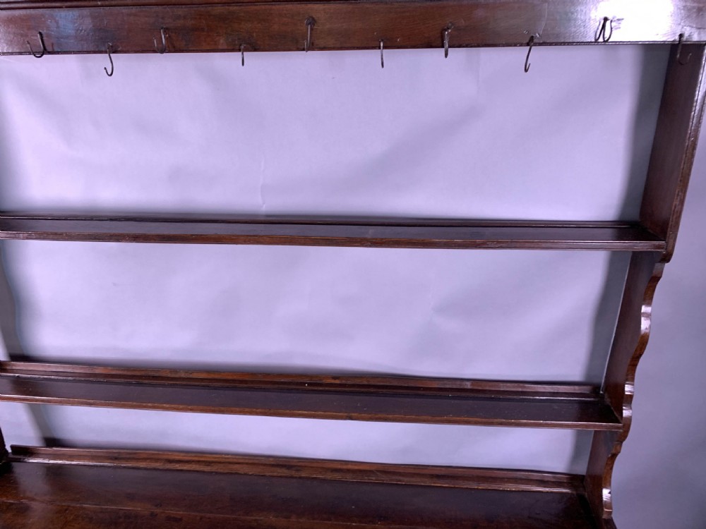 An 18th-century oak Welsh dresser featuring an open rack top with plate hooks, a central base with multiple drawers, and a lower pot board shelf. View XVI