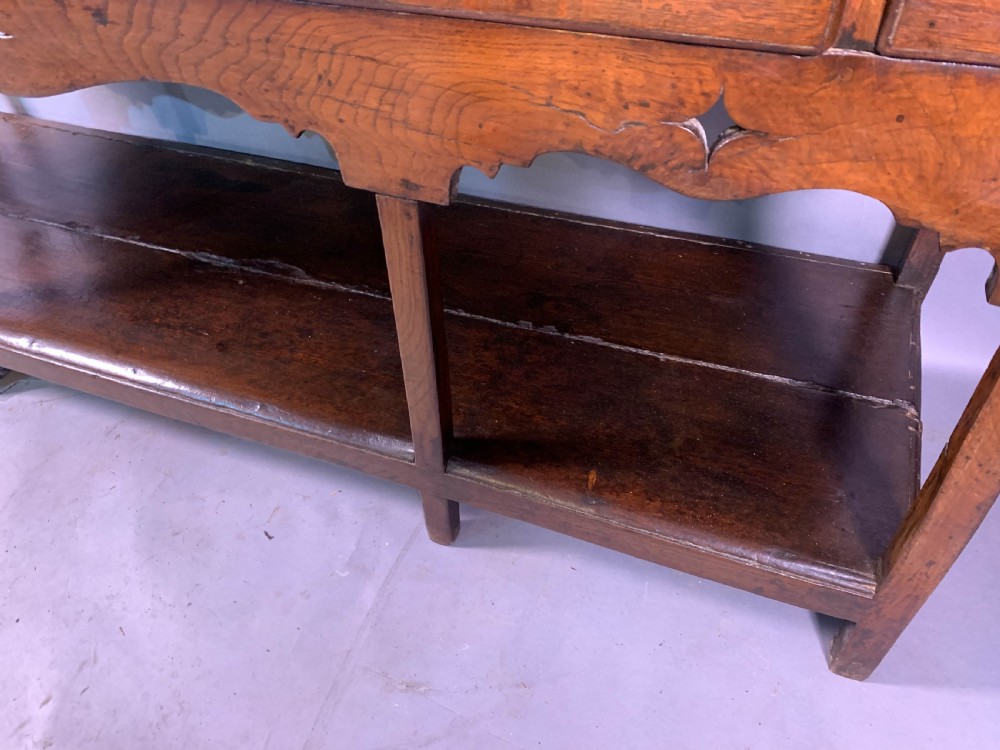 An 18th-century oak Welsh dresser featuring an open rack top with plate hooks, a central base with multiple drawers, and a lower pot board shelf. View XVII