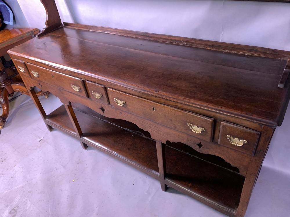 An 18th-century oak Welsh dresser featuring an open rack top with plate hooks, a central base with multiple drawers, and a lower pot board shelf. View XIX