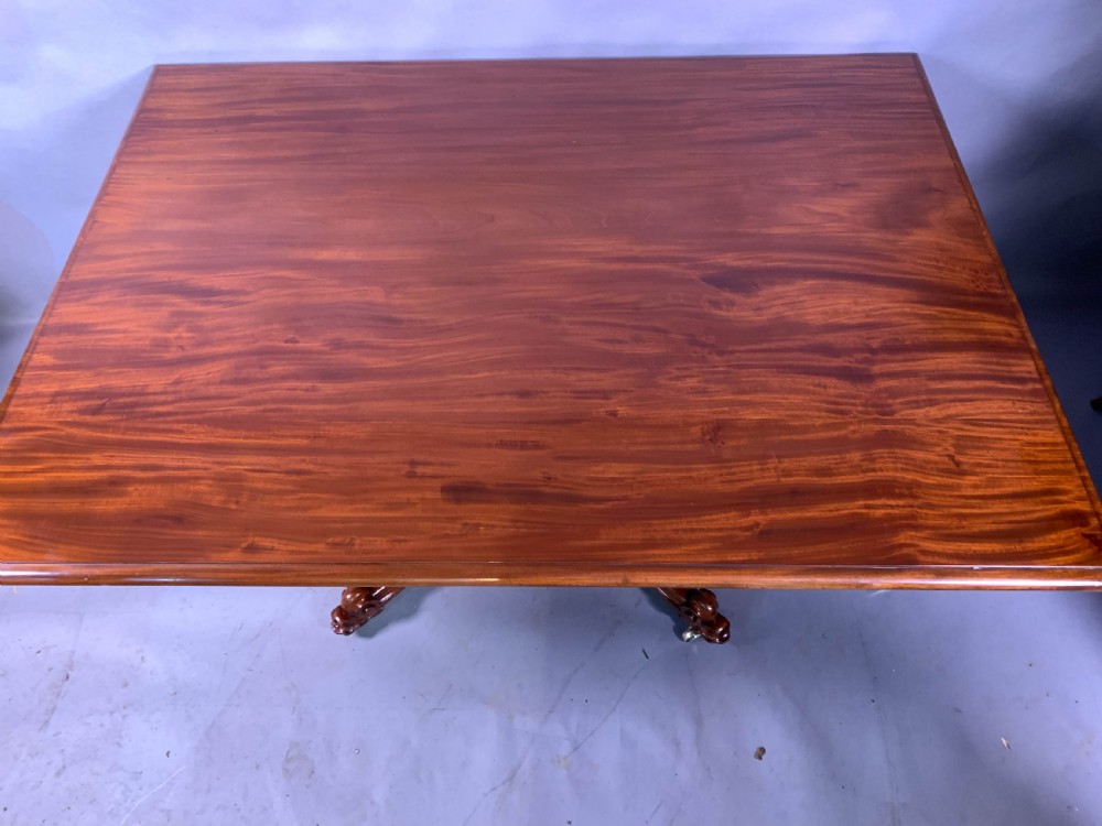 A rectangular mahogany breakfast dining table featuring a polished flame mahogany top set upon a central carved pedestal with splayed legs and brass castors. View III