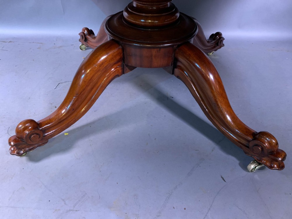 A rectangular mahogany breakfast dining table featuring a polished flame mahogany top set upon a central carved pedestal with splayed legs and brass castors. View V