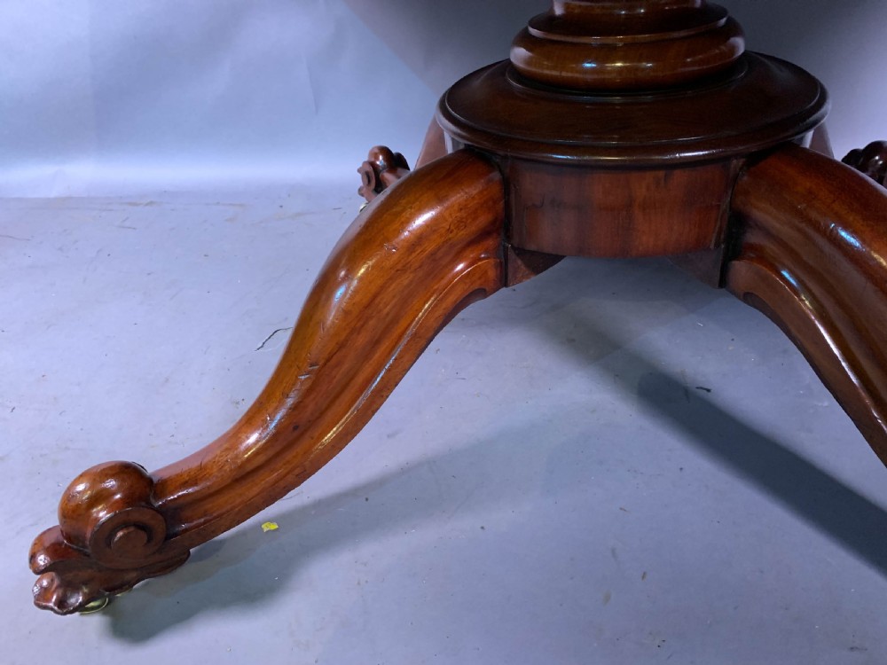 A rectangular mahogany breakfast dining table featuring a polished flame mahogany top set upon a central carved pedestal with splayed legs and brass castors. View VII