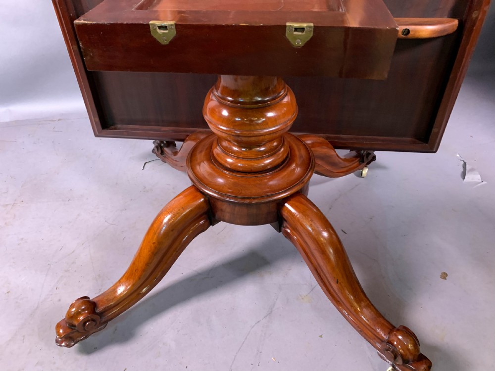 A rectangular mahogany breakfast dining table featuring a polished flame mahogany top set upon a central carved pedestal with splayed legs and brass castors. View X