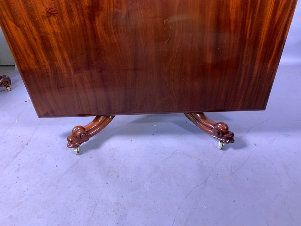 A rectangular mahogany breakfast dining table featuring a polished flame mahogany top set upon a central carved pedestal with splayed legs and brass castors. View XIII