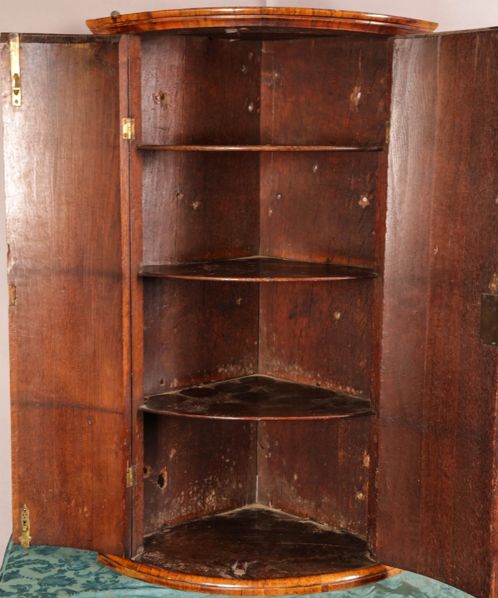 An eighteenth-century English bow-fronted corner cupboard crafted from figure-grained burr walnut with twin doors and a central brass escutcheon. View VII