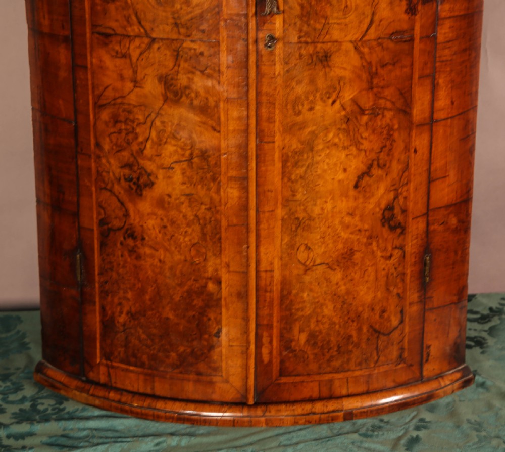 An eighteenth-century English bow-fronted corner cupboard crafted from figure-grained burr walnut with twin doors and a central brass escutcheon. View VIII
