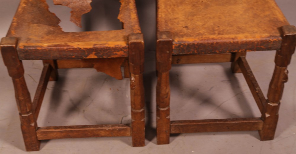 A pair of 1930s Arts and Crafts English oak side chairs featuring solid backs with cut-out handles, turned front legs with signature carved mouse motifs, and worn brown leather seats. View II