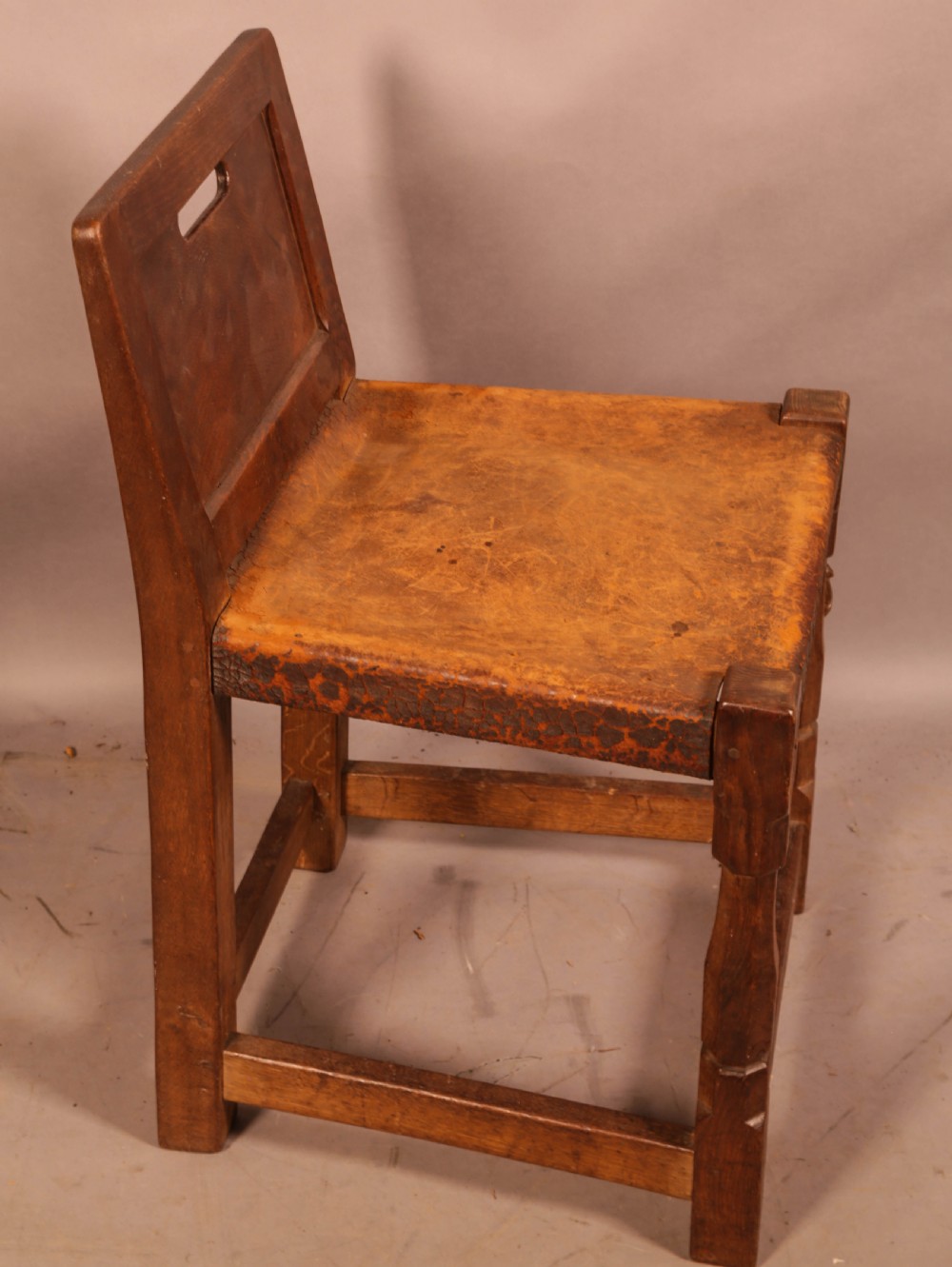 A pair of 1930s Arts and Crafts English oak side chairs featuring solid backs with cut-out handles, turned front legs with signature carved mouse motifs, and worn brown leather seats. View IV