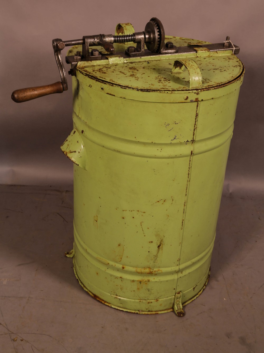 A pale green cylindrical metal honey separator with a top-mounted cast iron hand-crank mechanism and wooden handle.