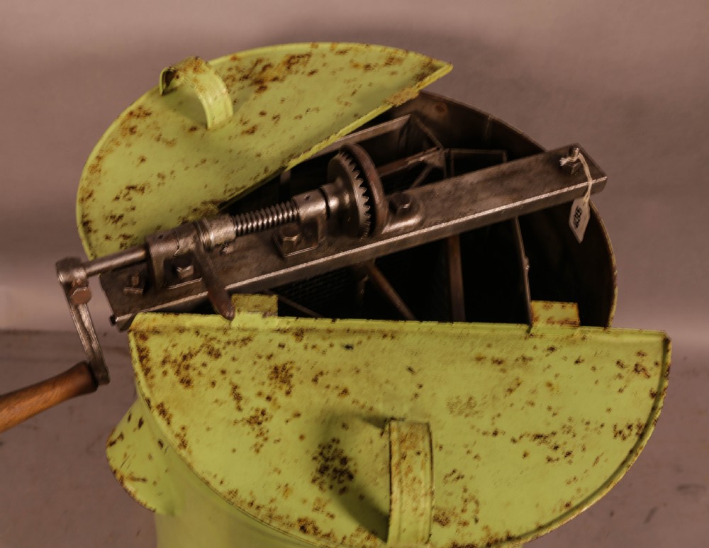 A pale green cylindrical metal honey separator with a top-mounted cast iron hand-crank mechanism and wooden handle. View III