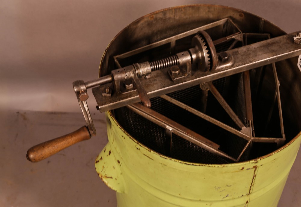 A pale green cylindrical metal honey separator with a top-mounted cast iron hand-crank mechanism and wooden handle. View IV