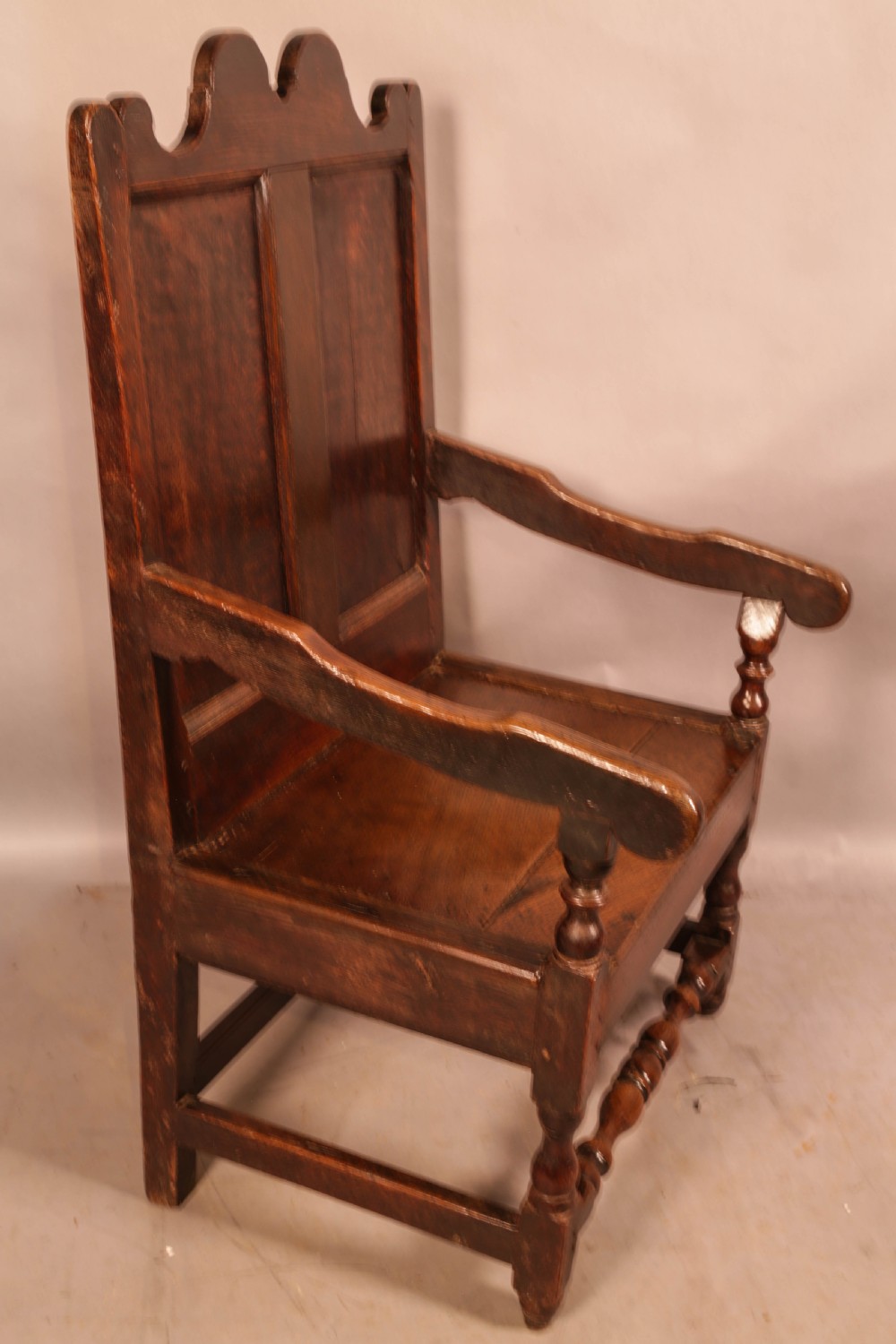 A 17th-century solid oak armchair featuring a panelled backrest with a shaped cresting rail, shaped arms, turned front legs, and plain stretchers.