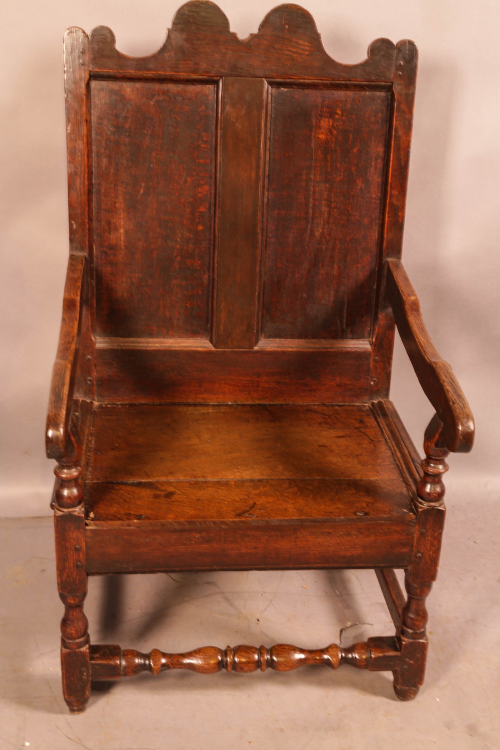 A 17th-century solid oak armchair featuring a panelled backrest with a shaped cresting rail, shaped arms, turned front legs, and plain stretchers. View II