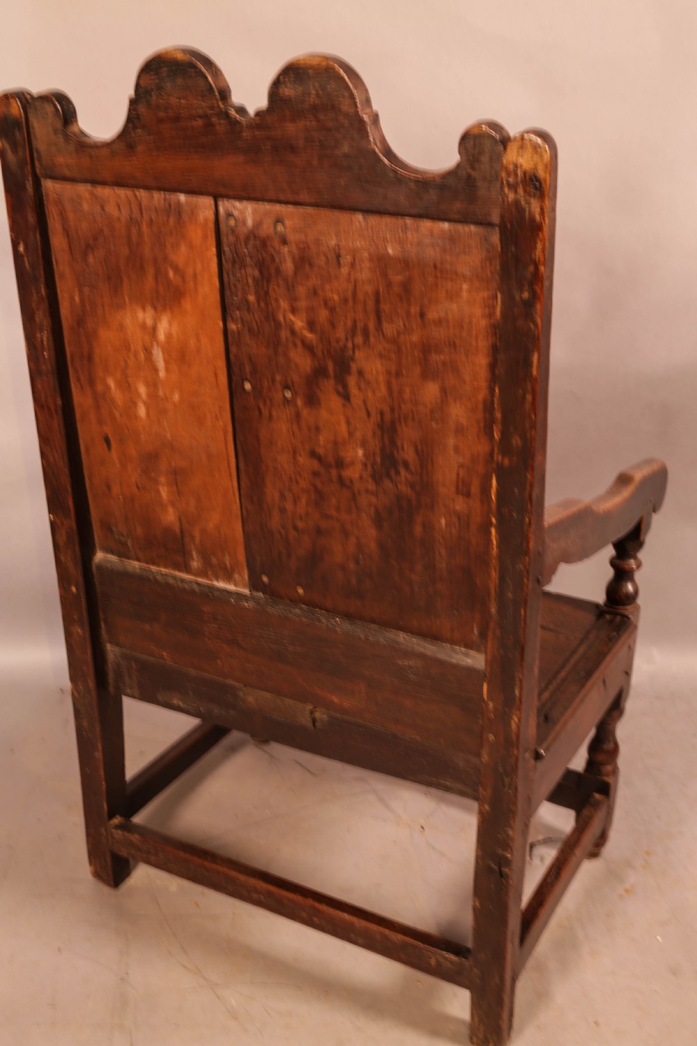 A 17th-century solid oak armchair featuring a panelled backrest with a shaped cresting rail, shaped arms, turned front legs, and plain stretchers. View III