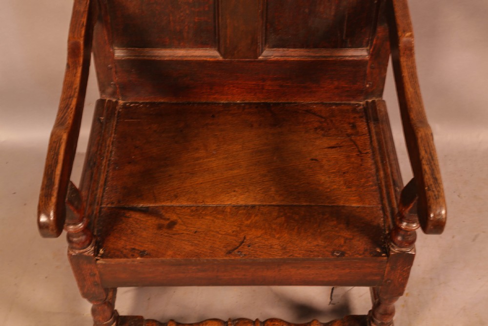 A 17th-century solid oak armchair featuring a panelled backrest with a shaped cresting rail, shaped arms, turned front legs, and plain stretchers. View IV