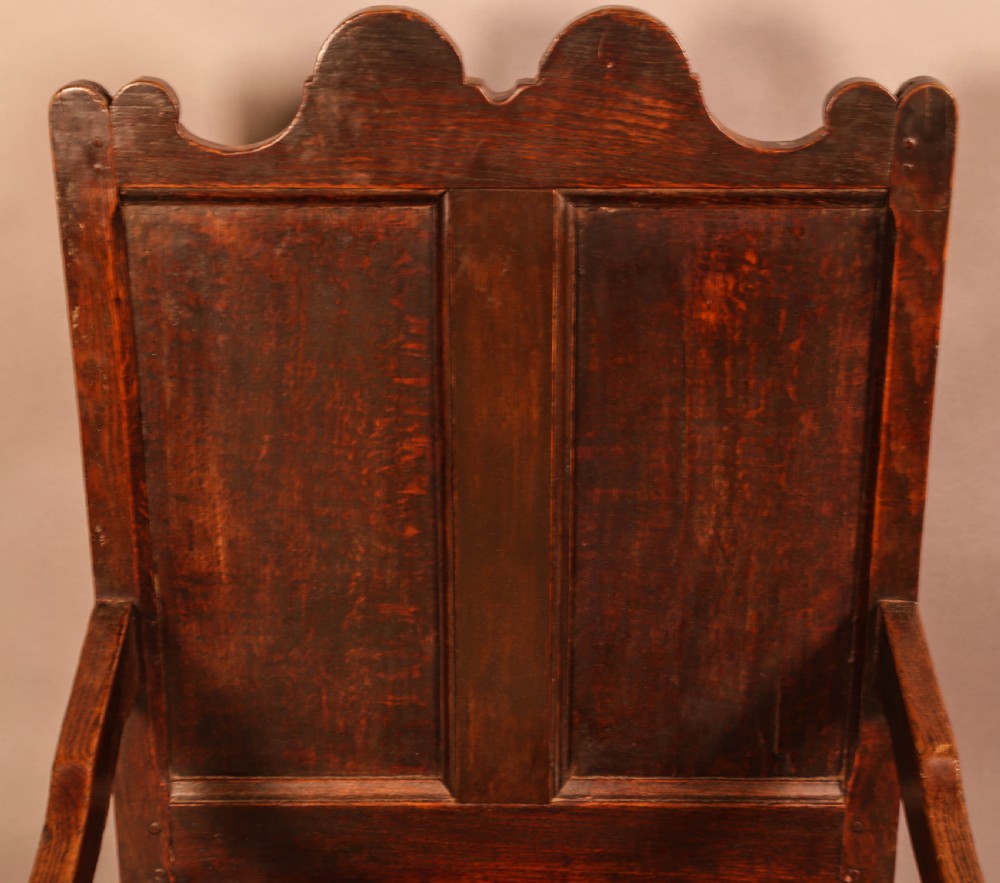 A 17th-century solid oak armchair featuring a panelled backrest with a shaped cresting rail, shaped arms, turned front legs, and plain stretchers. View VI