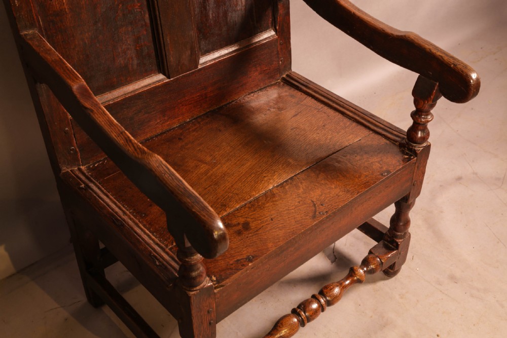 A 17th-century solid oak armchair featuring a panelled backrest with a shaped cresting rail, shaped arms, turned front legs, and plain stretchers. View VIII