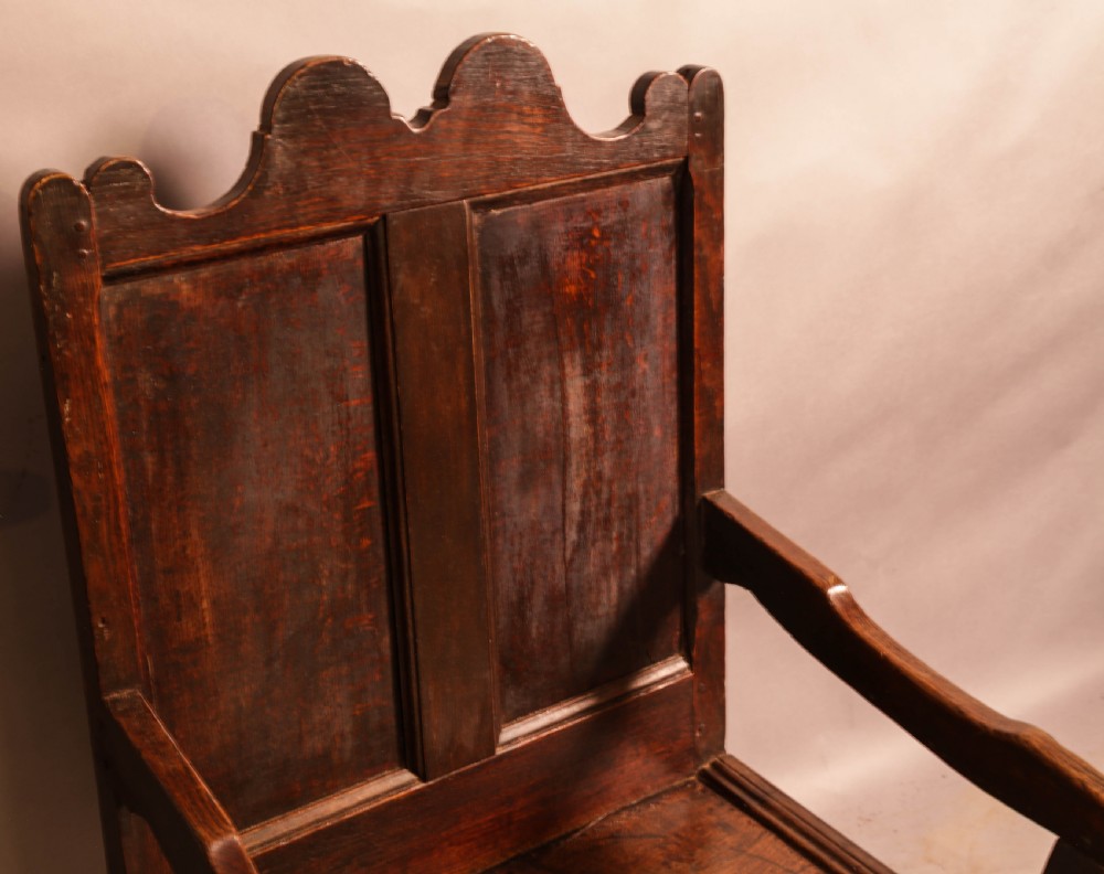 A 17th-century solid oak armchair featuring a panelled backrest with a shaped cresting rail, shaped arms, turned front legs, and plain stretchers. View IX