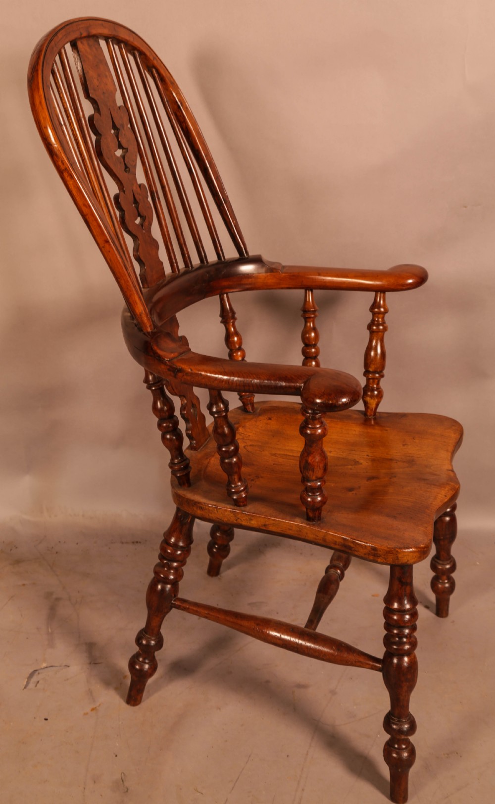An antique yew wood Windsor armchair featuring a bowed hoop back, pierced splat, turned legs, and a solid elm seat.