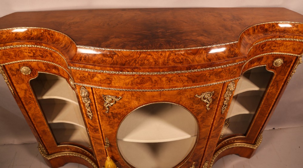 A serpentine-front Victorian burr walnut credenza featuring glazed doors, gilt bronze ormolu mounts, and intricate wood figuring. View VII