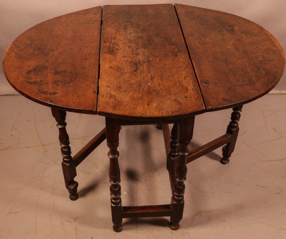 An antique dark oak gateleg table with turned legs and a drop-leaf oval top. View II