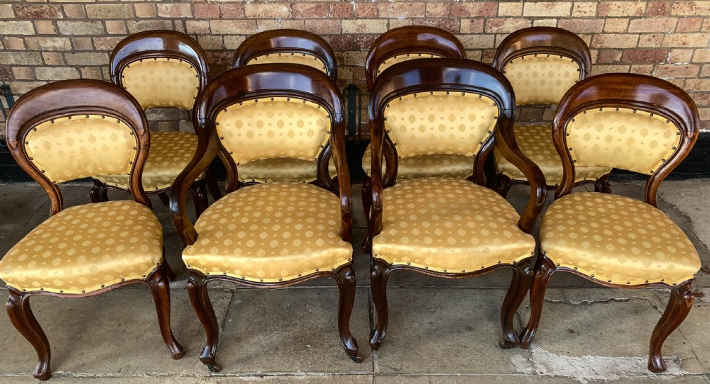 A set of eight Victorian mahogany dining chairs featuring gold patterned fabric upholstery, balloon backs, and cabriole legs.