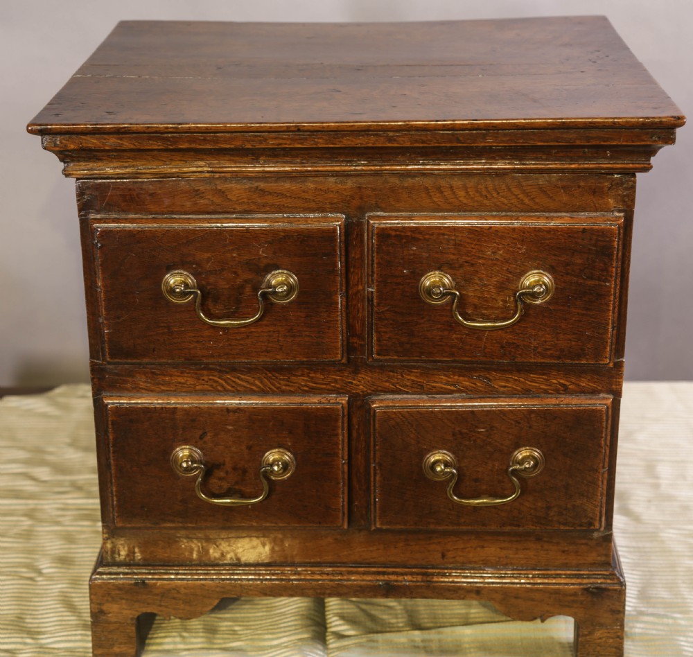 An 18th-century oak close stool designed with four faux drawer fronts, brass drop handles, and bracket feet.
