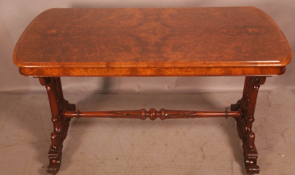 A Victorian burr walnut window table with a rectangular figured top, carved trestle supports, and a turned central stretcher.
