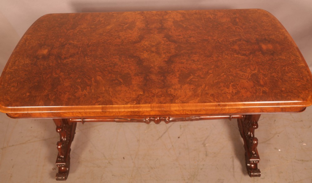 A Victorian burr walnut window table with a rectangular figured top, carved trestle supports, and a turned central stretcher. View II