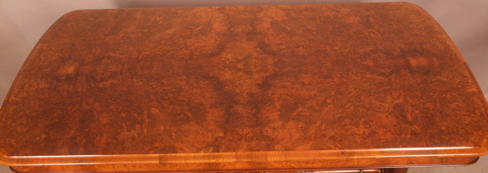 A Victorian burr walnut window table with a rectangular figured top, carved trestle supports, and a turned central stretcher. View III