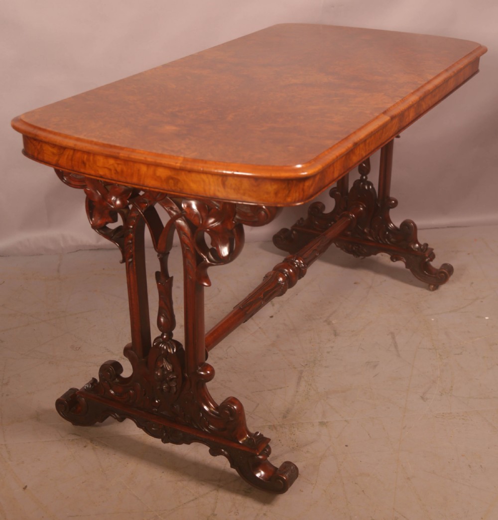 A Victorian burr walnut window table with a rectangular figured top, carved trestle supports, and a turned central stretcher. View IV