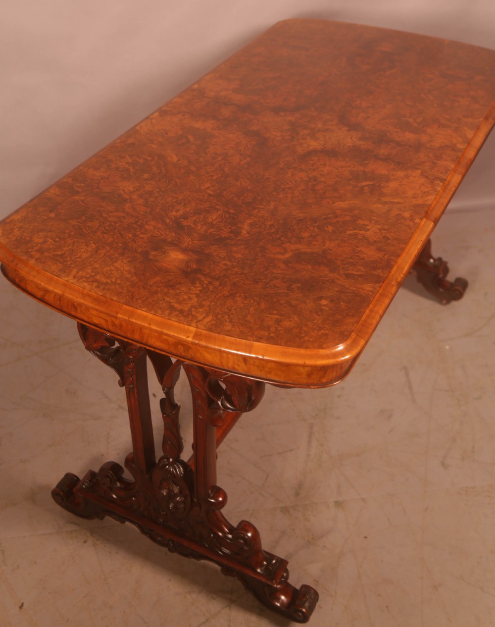 A Victorian burr walnut window table with a rectangular figured top, carved trestle supports, and a turned central stretcher. View V