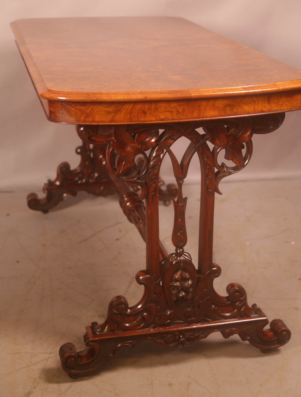 A Victorian burr walnut window table with a rectangular figured top, carved trestle supports, and a turned central stretcher. View VII