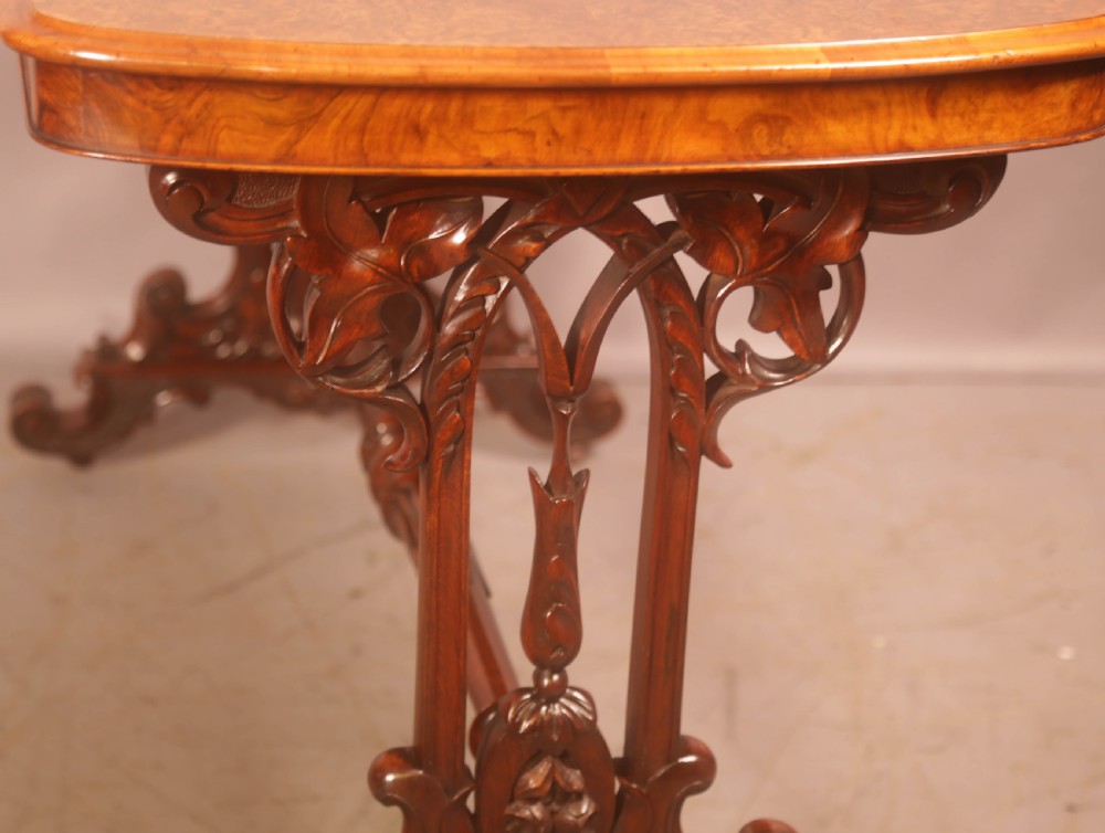 A Victorian burr walnut window table with a rectangular figured top, carved trestle supports, and a turned central stretcher. View X
