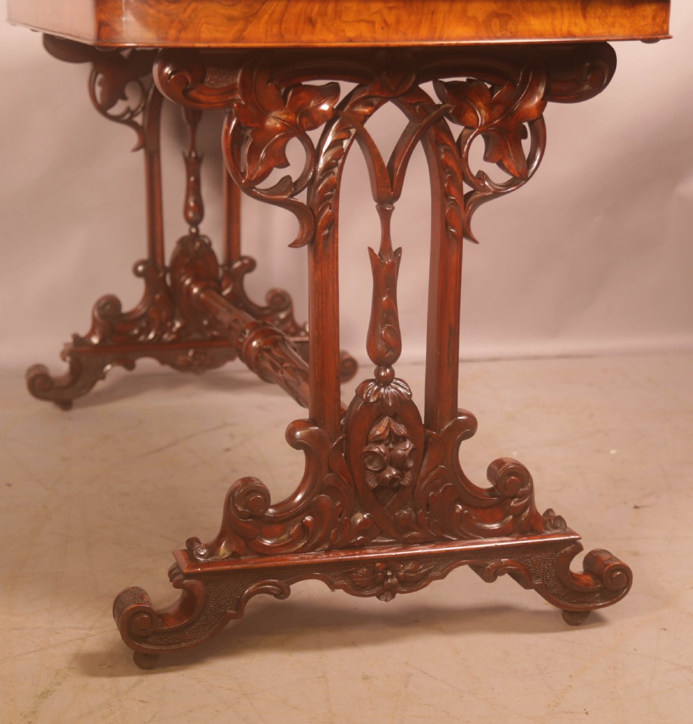 A Victorian burr walnut window table with a rectangular figured top, carved trestle supports, and a turned central stretcher. View XI