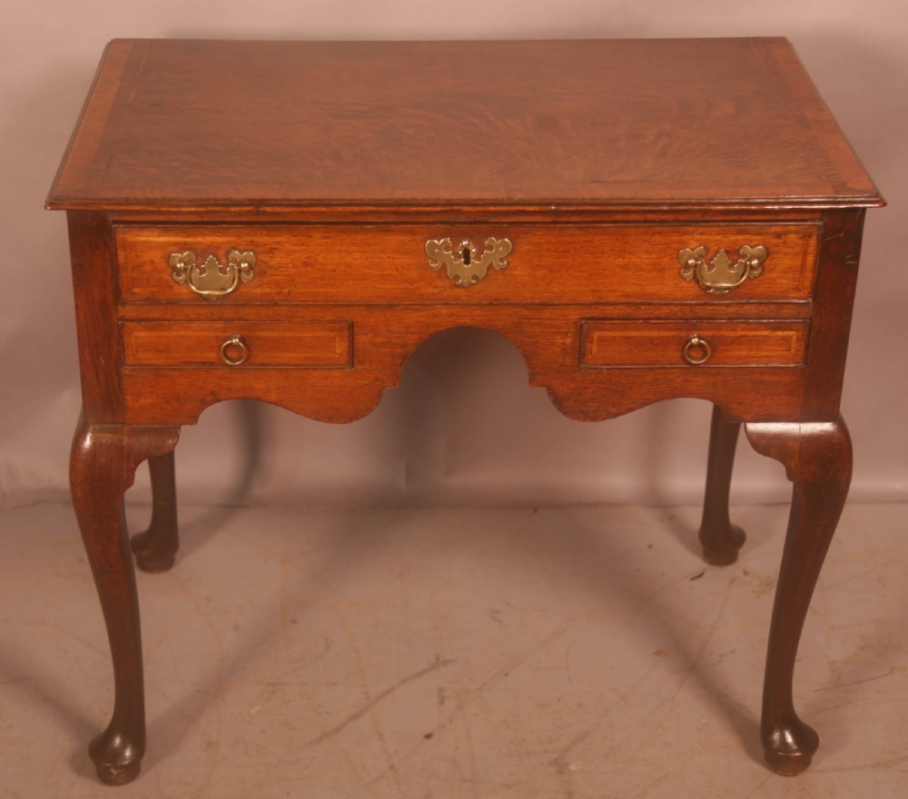 An eighteenth-century oak side table featuring a rectangular top, cabriole legs, and three drawers with brass drop handles.