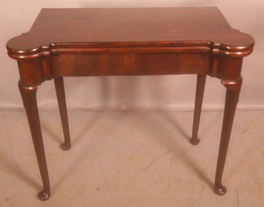 A mid-18th century Georgian mahogany fold-over card table featuring projecting rounded corners, a smooth apron, and slender cabriole legs terminating in pad feet.