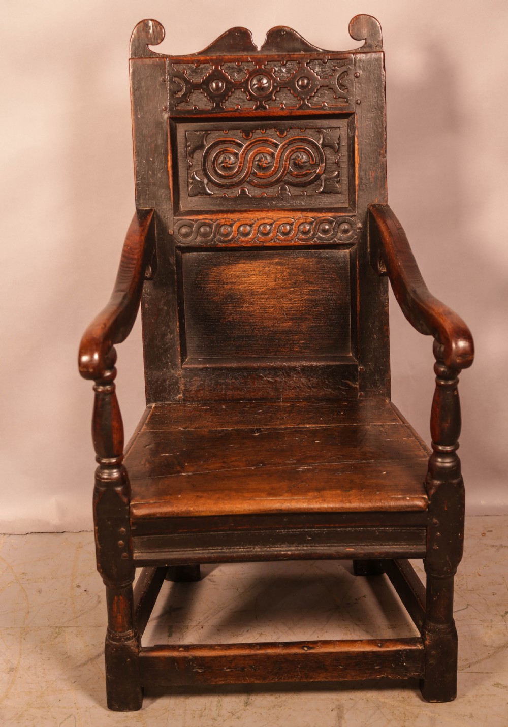 A dark oak 17th-century wainscot armchair with a carved panelled backrest, turned supports, and a solid wooden seat.