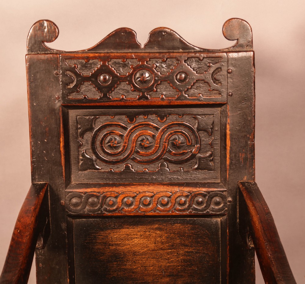 A dark oak 17th-century wainscot armchair with a carved panelled backrest, turned supports, and a solid wooden seat. View V