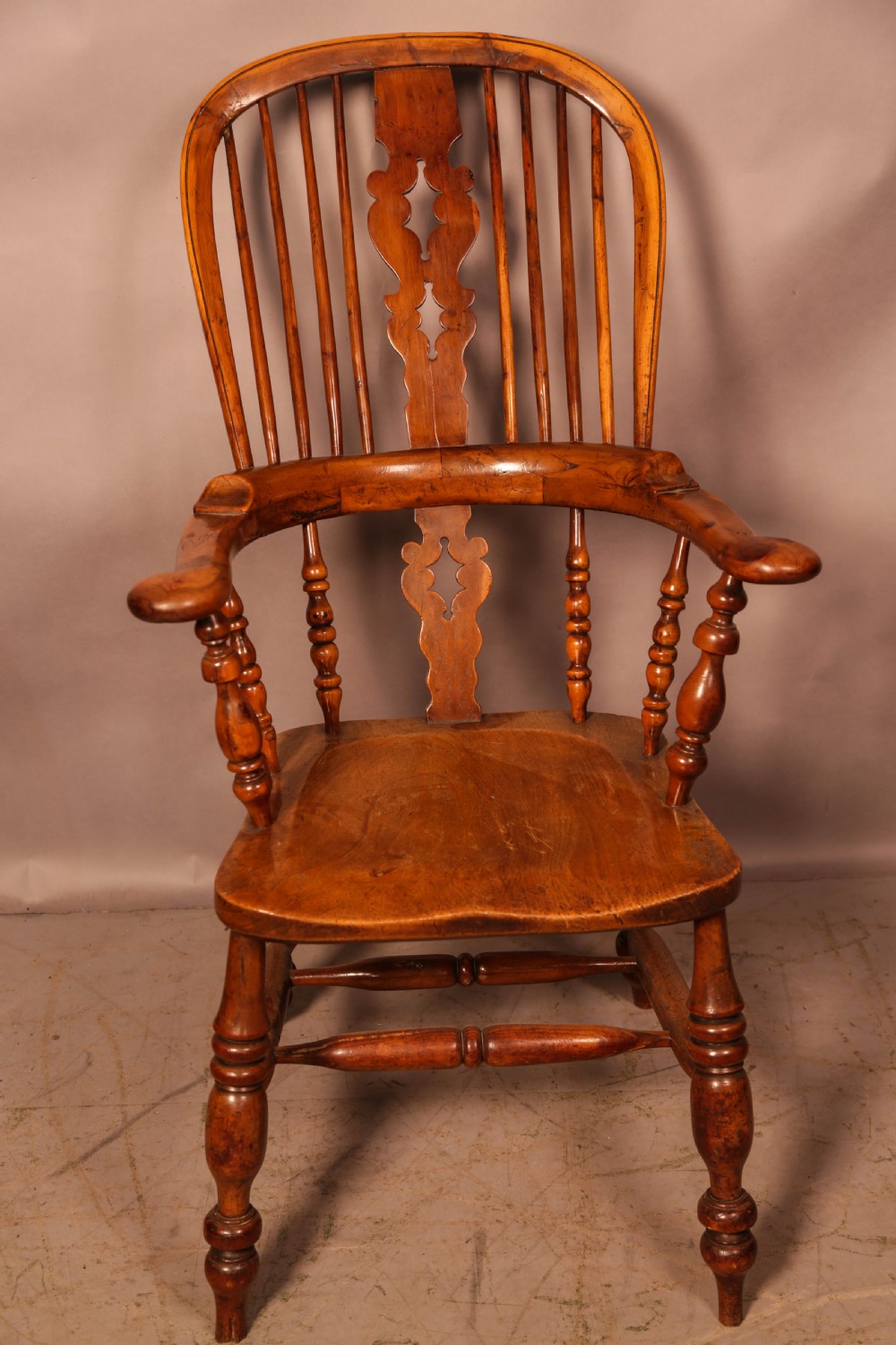 An antique English yew wood broad arm Windsor chair featuring a hooped back with a central pierced splat, turned legs, and a solid wood saddle seat. View II