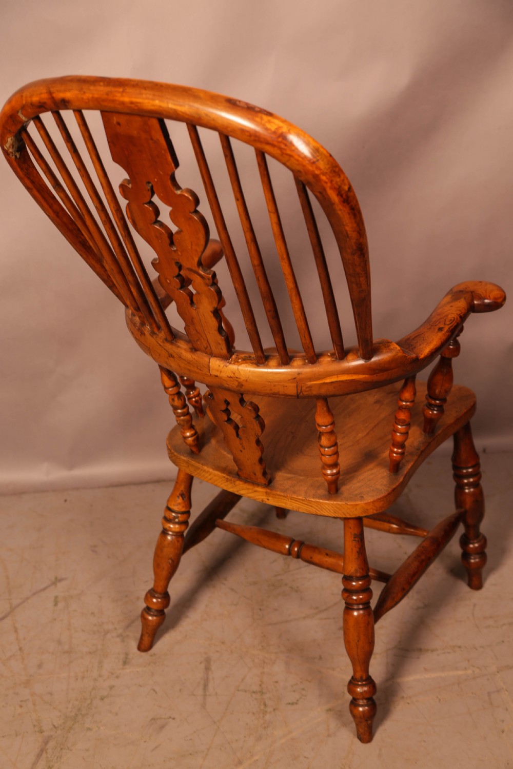 An antique English yew wood broad arm Windsor chair featuring a hooped back with a central pierced splat, turned legs, and a solid wood saddle seat. View III