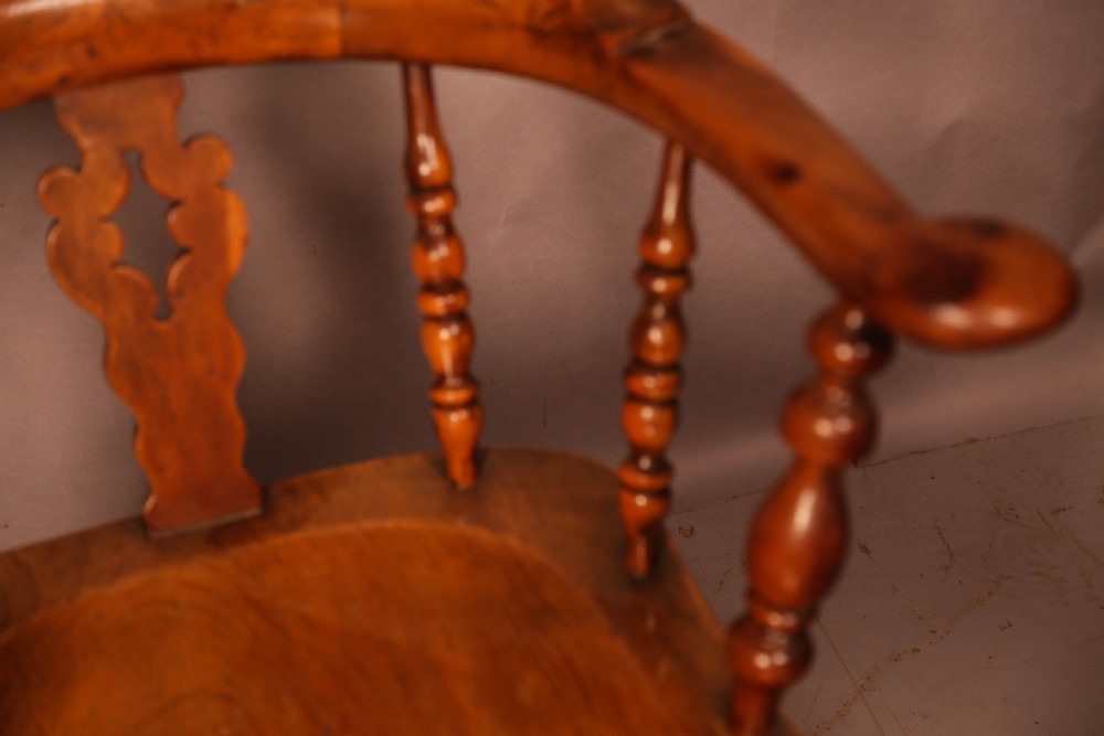 An antique English yew wood broad arm Windsor chair featuring a hooped back with a central pierced splat, turned legs, and a solid wood saddle seat. View IV