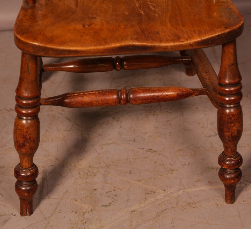 An antique English yew wood broad arm Windsor chair featuring a hooped back with a central pierced splat, turned legs, and a solid wood saddle seat. View V