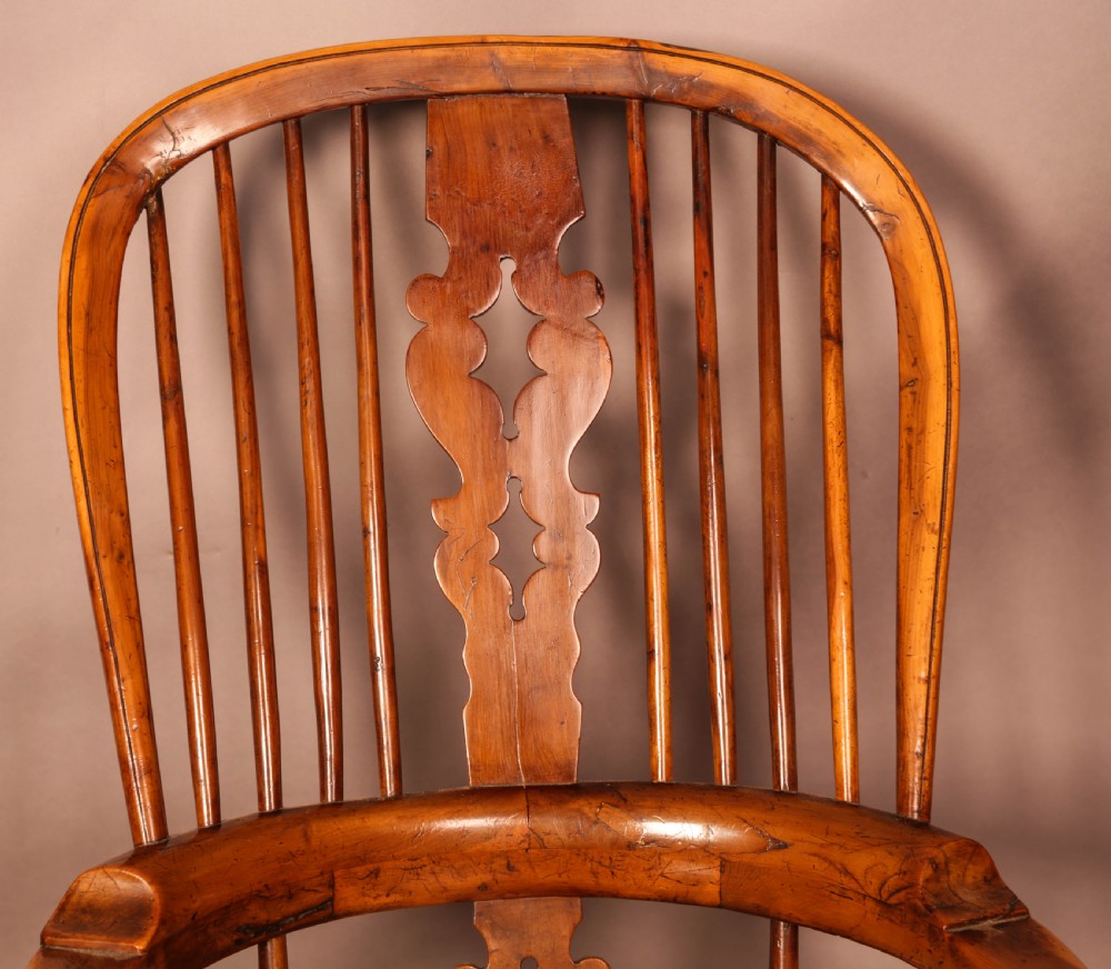 An antique English yew wood broad arm Windsor chair featuring a hooped back with a central pierced splat, turned legs, and a solid wood saddle seat. View VII