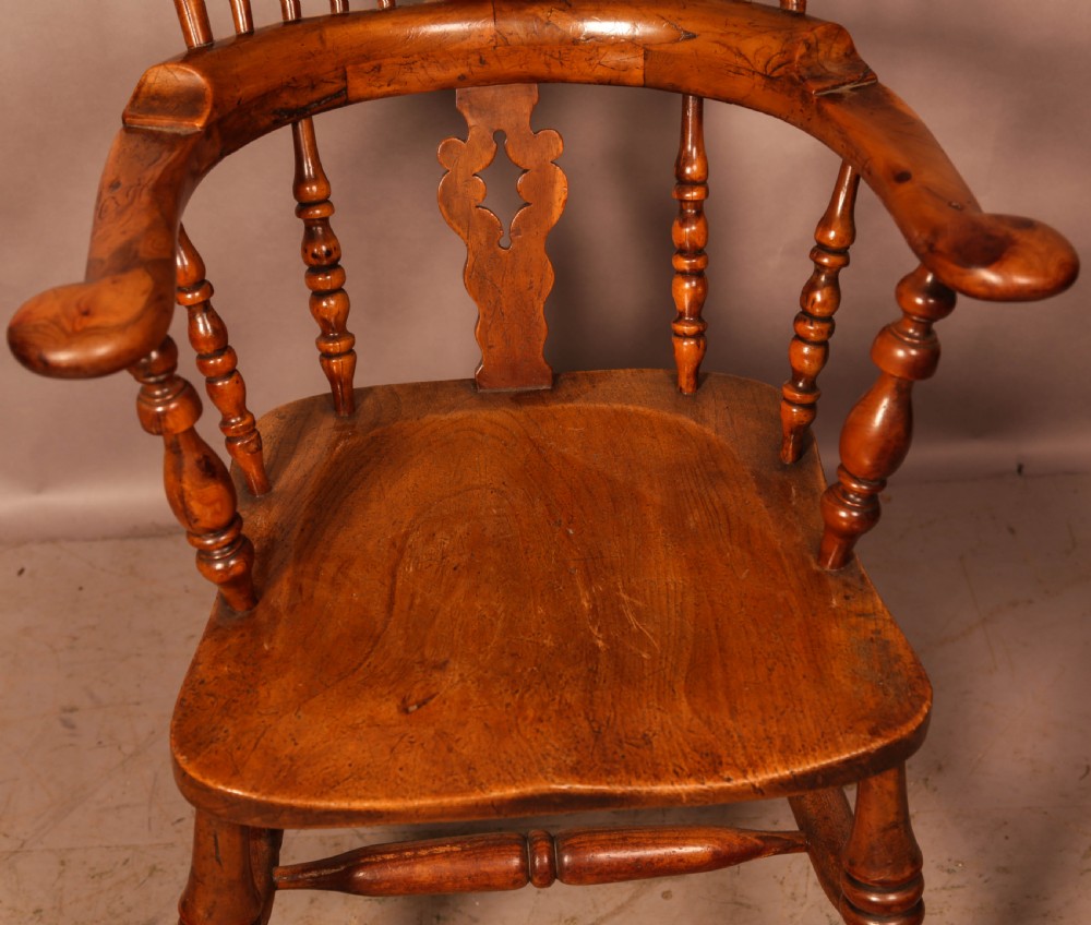 An antique English yew wood broad arm Windsor chair featuring a hooped back with a central pierced splat, turned legs, and a solid wood saddle seat. View VIII