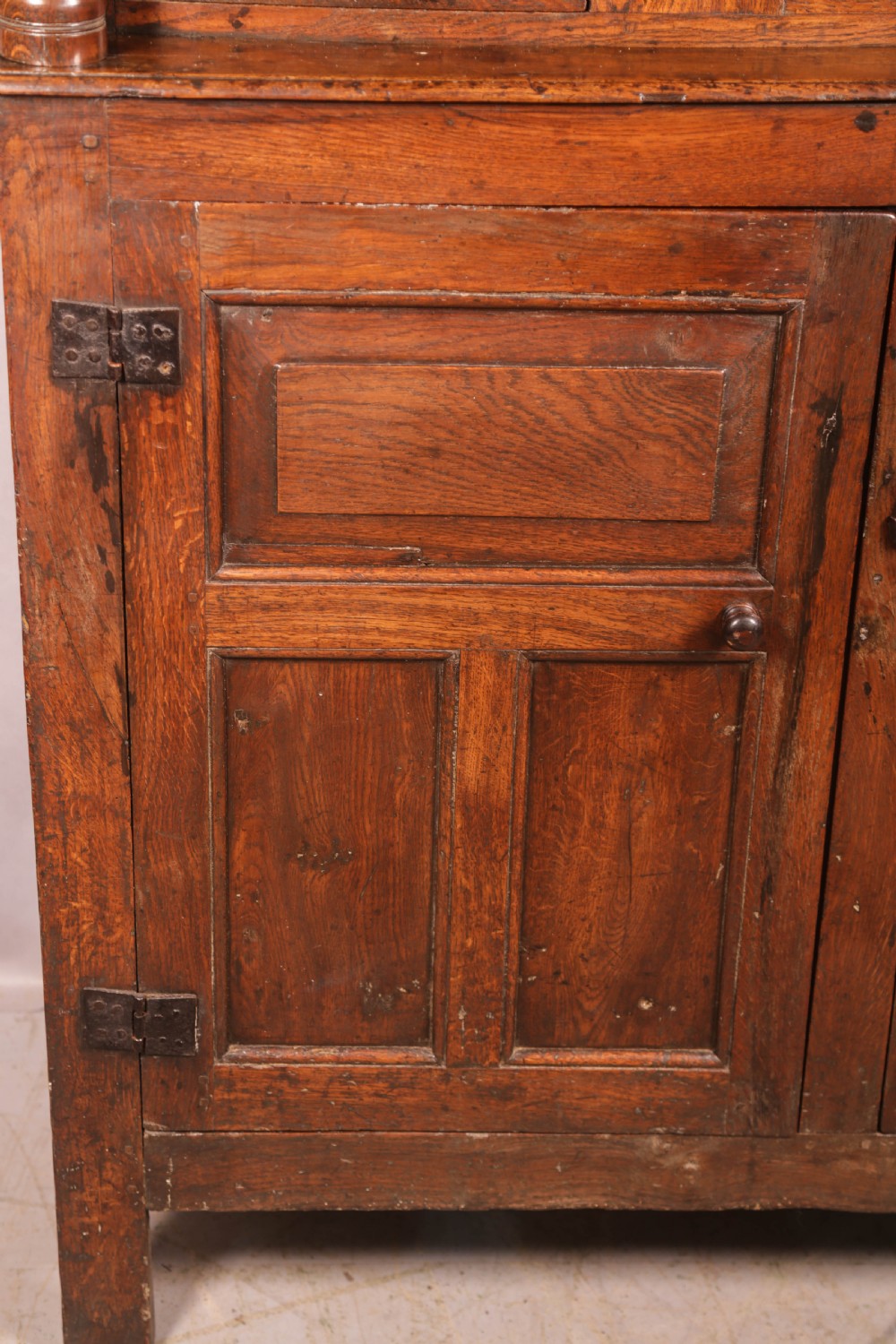 A front view of an 18th-century dark oak court cupboard featuring panelled doors, turned columns, and carved initials on the frieze. View XIII
