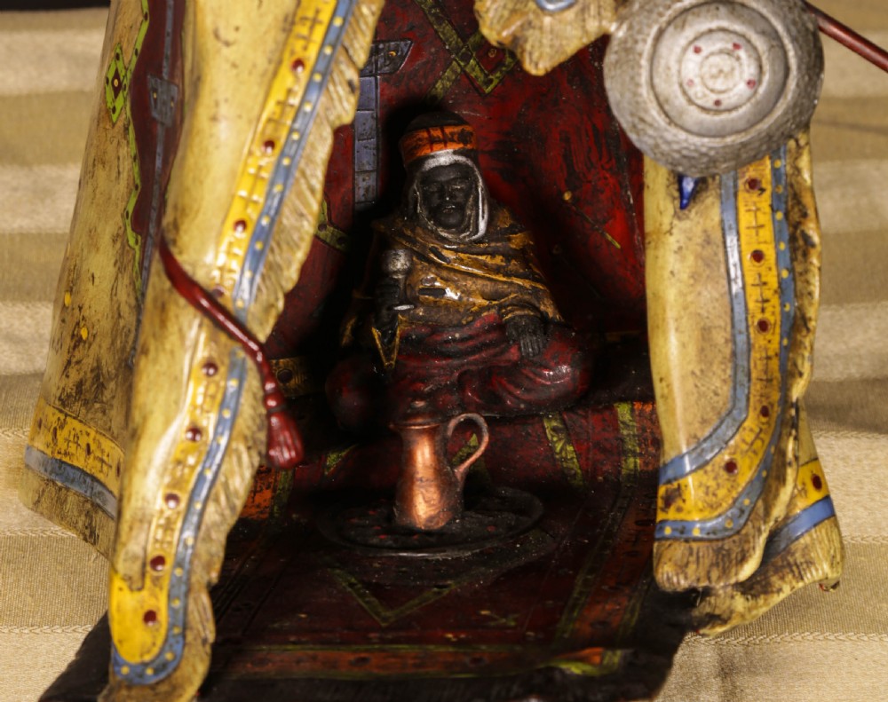A cold-painted bronze sculpture depicting a bedouin tent with patterned yellow draping, a green domed top, and accompanying miniature weapons. View VII
