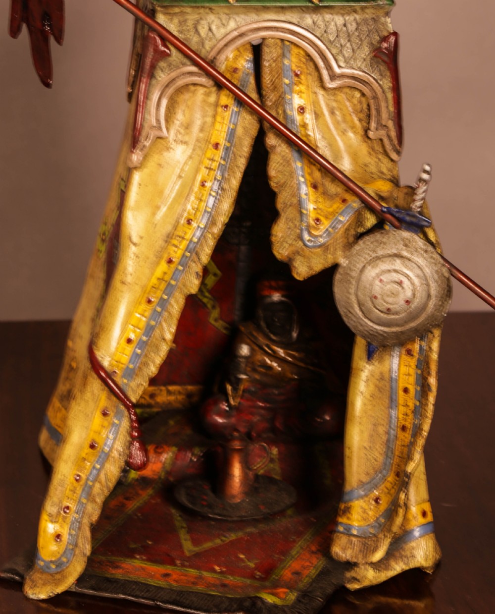 A cold-painted bronze sculpture depicting a bedouin tent with patterned yellow draping, a green domed top, and accompanying miniature weapons. View VIII